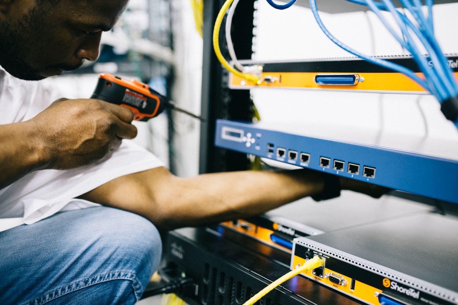 Technician using a cordless driver while working on cabling and equipment in a network rack